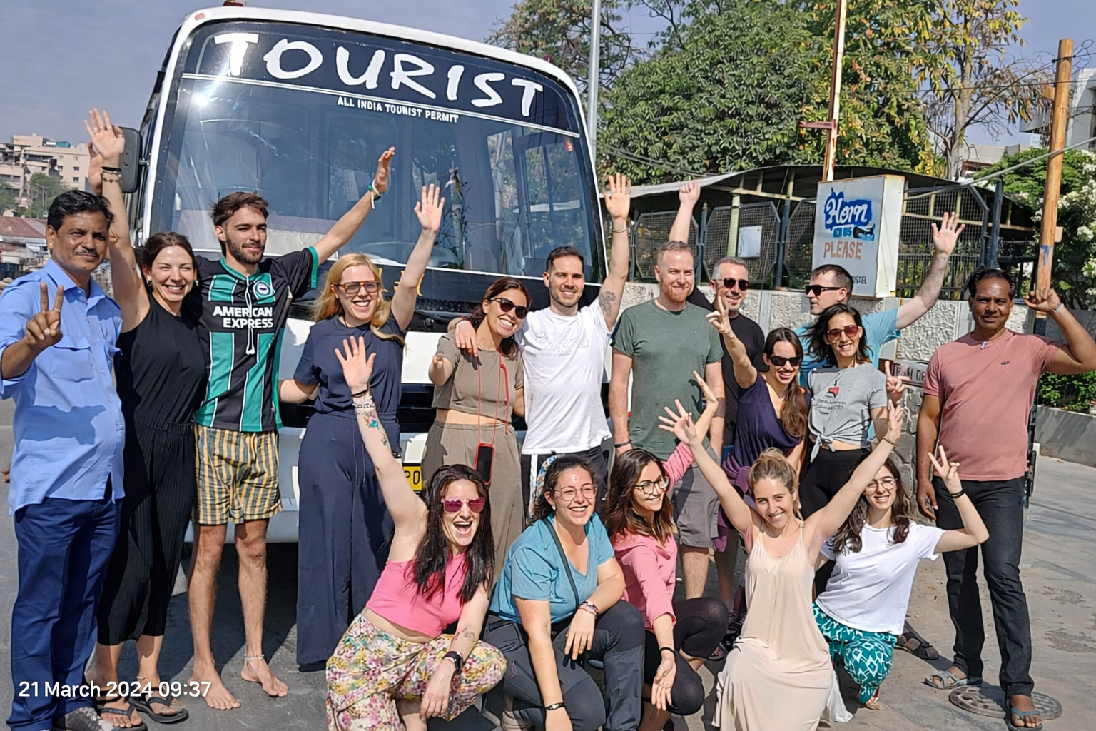 Group of international travelers with driver and guide posing in front of tourist bus during India tour