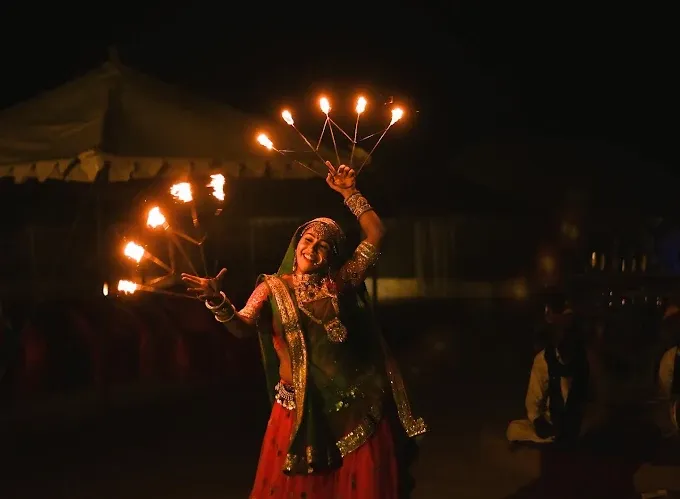 Traditional desert camp with cultural dancer performance under decorative lights at night