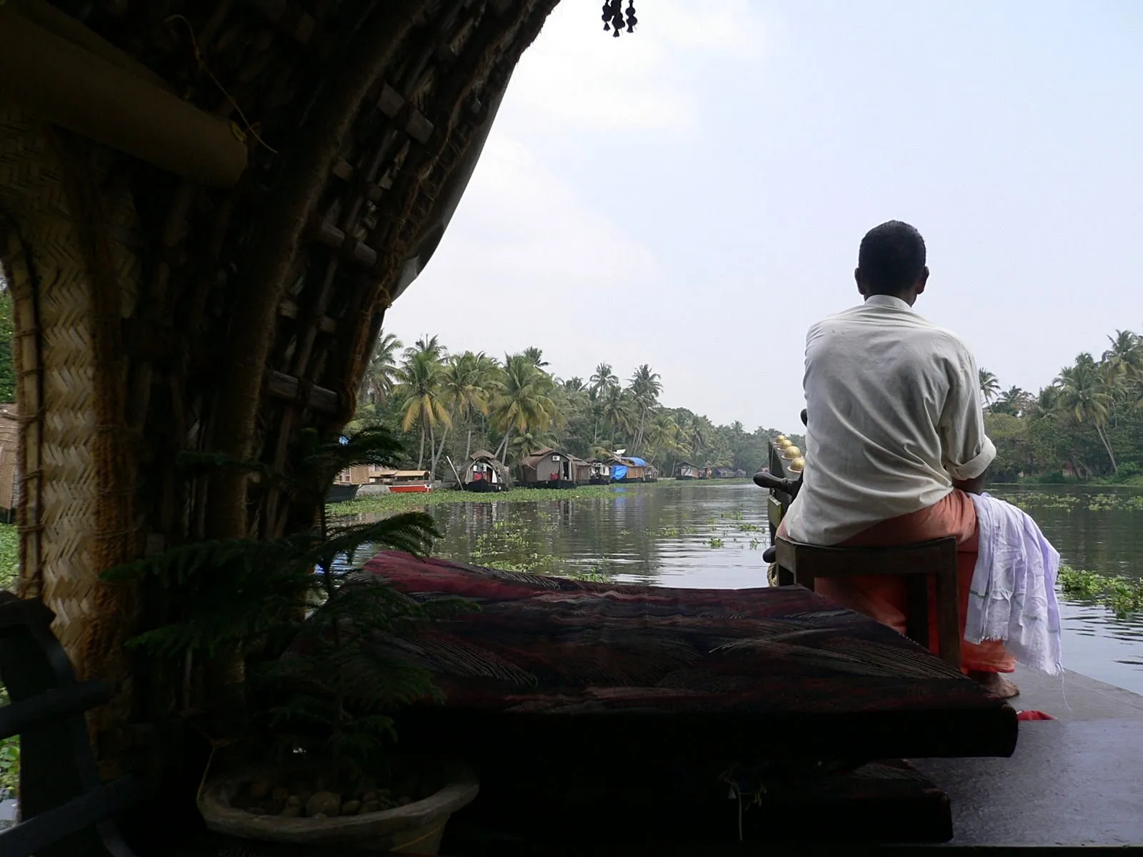 Back view of a houseboat driver navigating Kerala backwaters in our Kerala travel guide