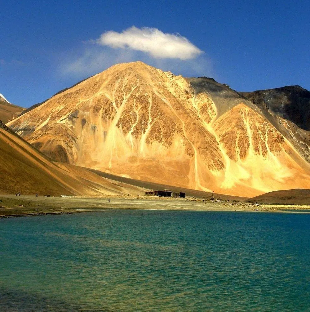 Sunrise over Pangong Lake in Ladakh with golden light illuminating the surrounding Himalayan mountains and calm blue water