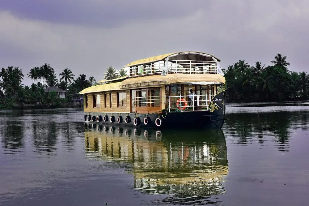 Luxury Kerala houseboat cruising in Alleppey backwaters at sunrise with calm water reflection and misty morning atmosphere